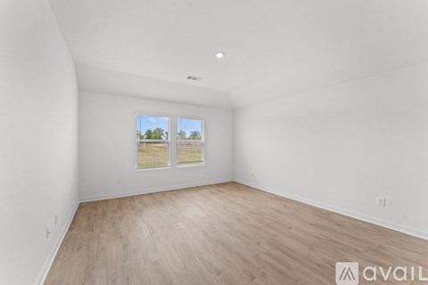 A room with wooden flooring and a window showing a view of trees.