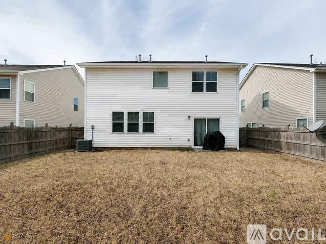 A white house with a black door and windows is surrounded by a fence and has a grassy yard.