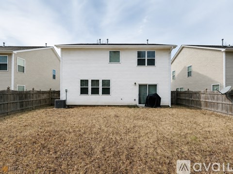 A white house with a black door and windows is surrounded by a fence and has a grassy yard.