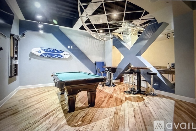 A pool table in a room with a wooden floor and a blue wall with a white X on it.