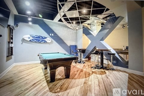 A pool table in a room with a wooden floor and a blue wall with a white X on it.