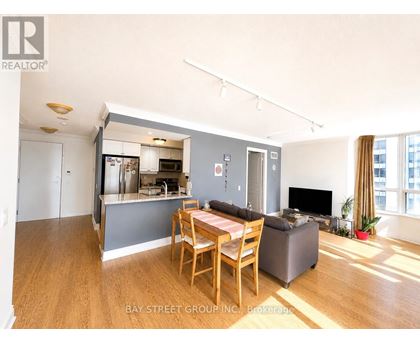 A living room with a dining table and chairs, a television, and a kitchen area in the background.