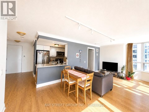 A living room with a dining table and chairs, a television, and a kitchen area in the background.