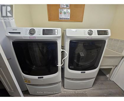 Two white ovens are in a room with a brown board on the wall.