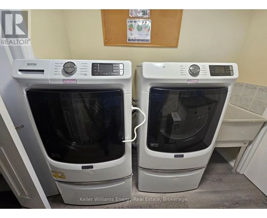 Two white ovens are in a room with a brown board on the wall.