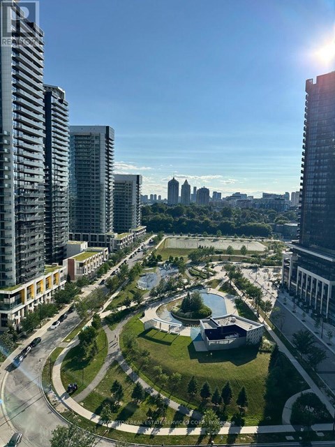 A sunny day in a city with tall buildings, a roundabout, and a green park.
