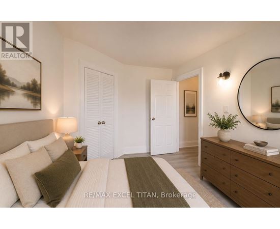 A well-lit bedroom with a large bed, a side table with a lamp, and a dresser with a mirror above it.