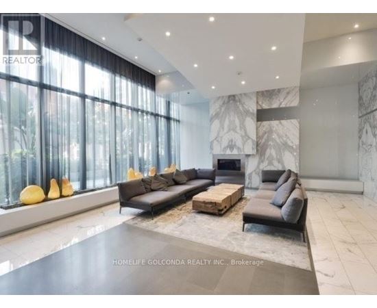 A spacious living room with a black sofa set and a marble fireplace.