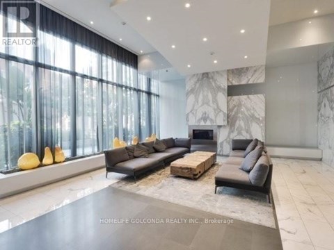 A spacious living room with a black sofa set and a marble fireplace.