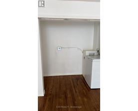 A white wall with a socket and a washing machine in a room with wooden flooring.