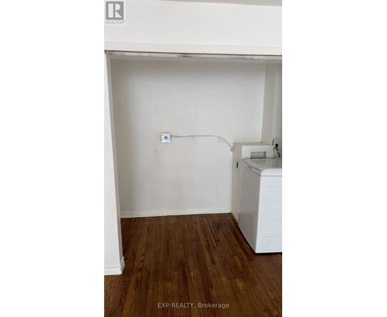 A white wall with a socket and a washing machine in a room with wooden flooring.
