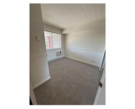 A room with a carpeted floor and a window with blinds.