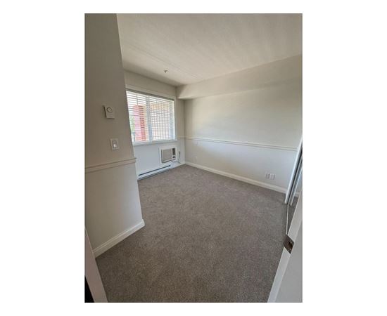 A room with a carpeted floor and a window with blinds.
