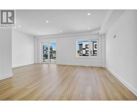 A spacious room with wooden flooring and two windows showing a view of buildings.