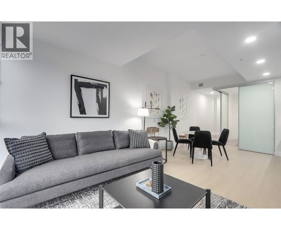 A living room with a grey couch, a coffee table, and a dining table with chairs.