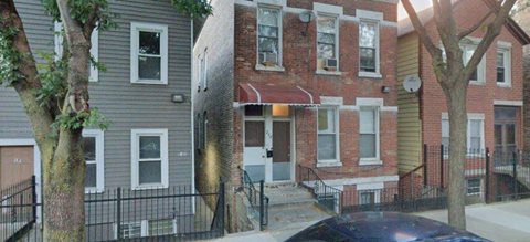 A black car is parked in front of a two-story building.