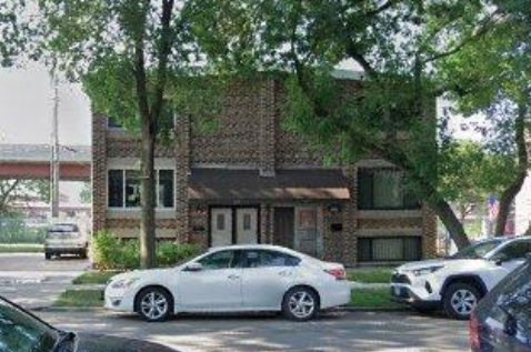 A white car is parked in front of a brick building.