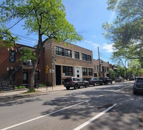 A street view with cars parked on the side of the road and a building with a yellow sign in the background.