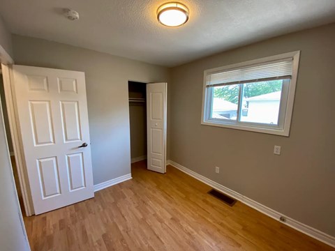 A room with a white door, a window, and a wooden floor.