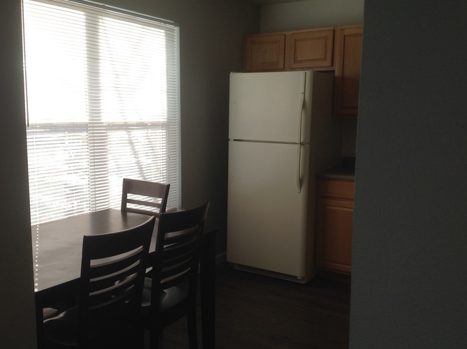 A white refrigerator is in a kitchen next to a table with two chairs.