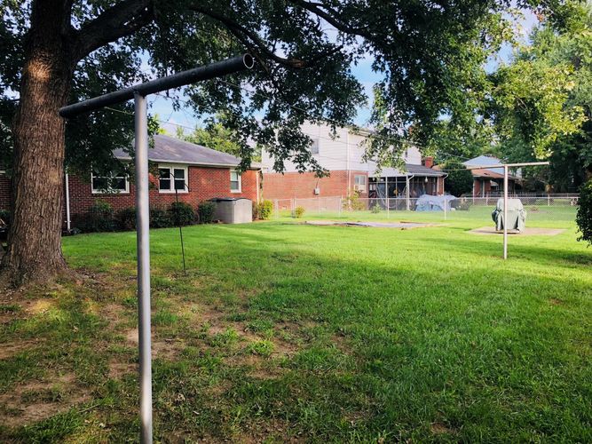 A swing set in a grassy yard with a tree and houses in the background.