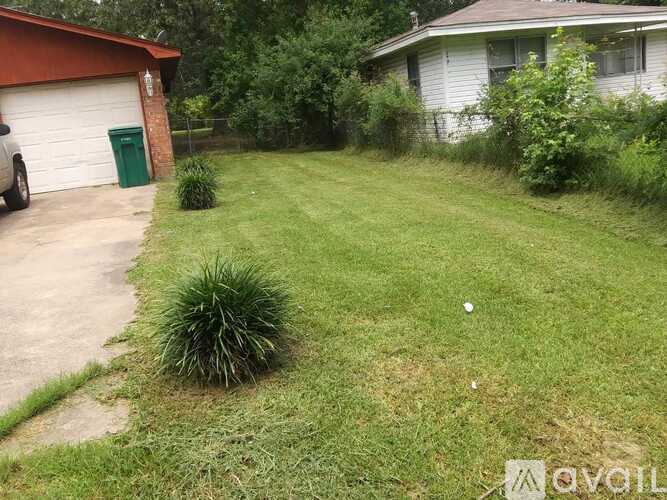 A backyard with a green trash can and a white house.