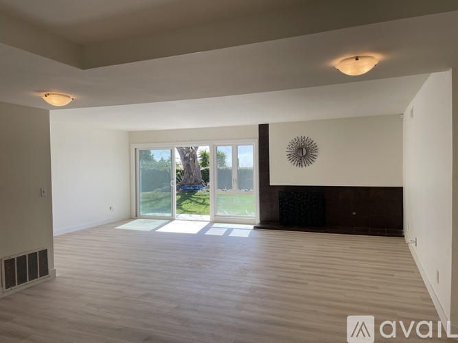 A spacious room with wooden flooring and a large window overlooking a garden.