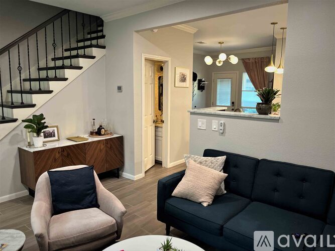 A living room with a black couch, a chair, and a staircase.