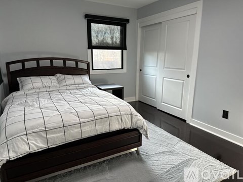 A bed with a white comforter and a wooden headboard sits in a room with a window and a door.