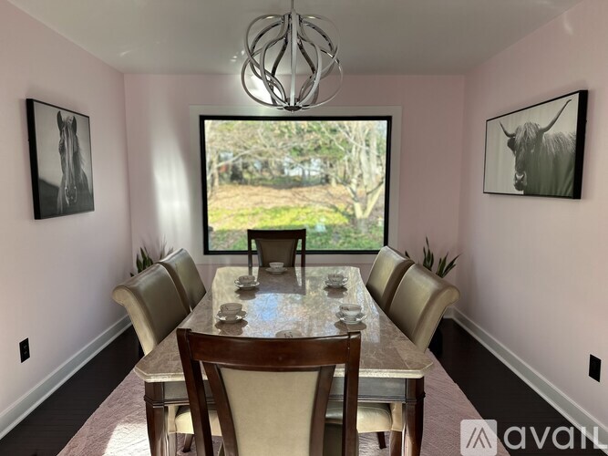 A dining room with a table set for six and a view of a garden outside the window.