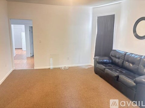 A living room with a black leather couch and a round mirror on the wall.