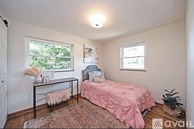 A bedroom with a pink bedspread and a rug on the floor.