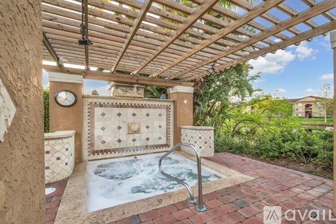 A hot tub is surrounded by a brick patio and a wooden pergola.