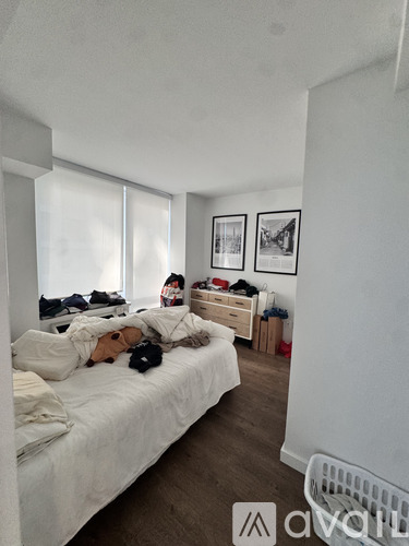 A woman is standing in a bedroom with a bed, dresser, and two pictures on the wall.