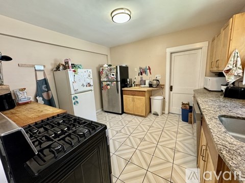 A kitchen with a black stove top oven, white fridge, and white trash can.