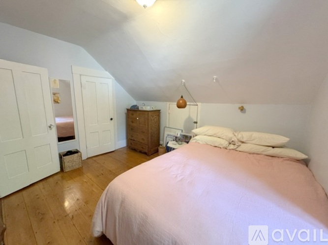 A bedroom with a bed, wooden dresser, and a window with blinds.