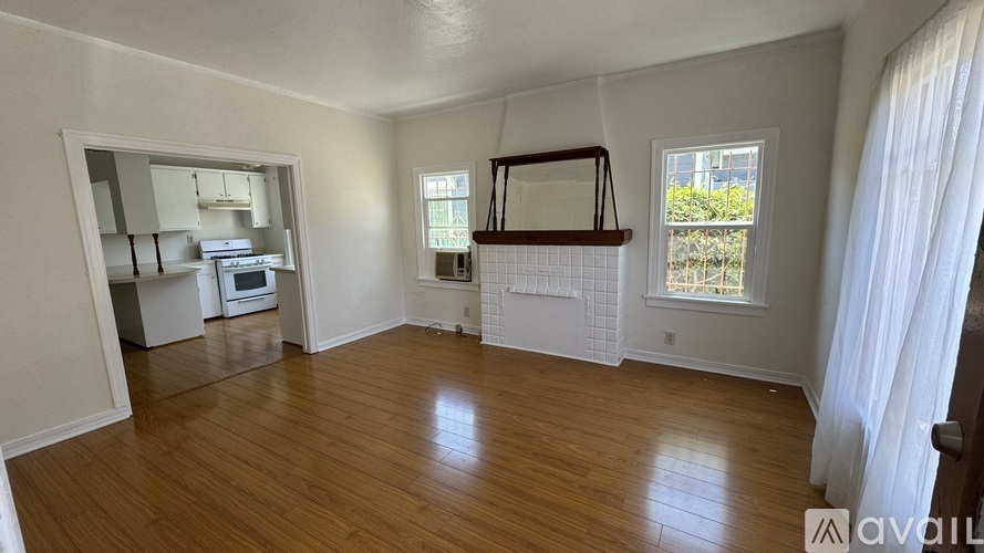 A room with wooden floors and white walls, a window with a view of greenery, and a balcony with a railing.