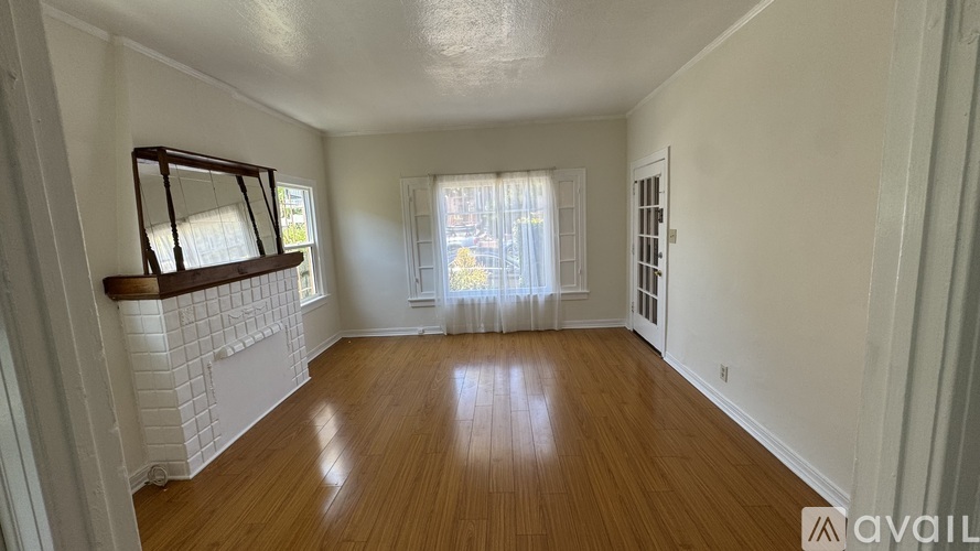 A room with wooden floors and white walls, with a window covered by white curtains.