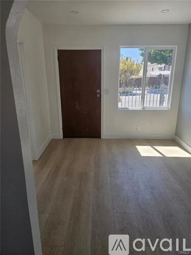 A room with a brown door and a window showing a fence and trees outside.