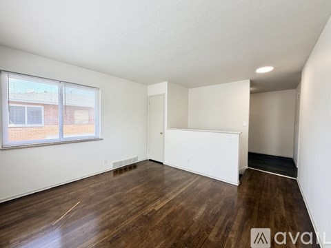A room with wooden floors and white walls, with a window on the left side.