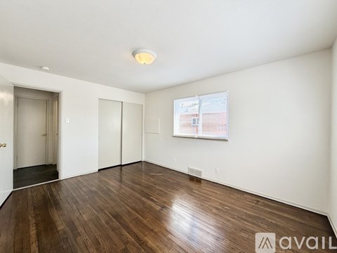 A room with wooden flooring and a white wall with a window.