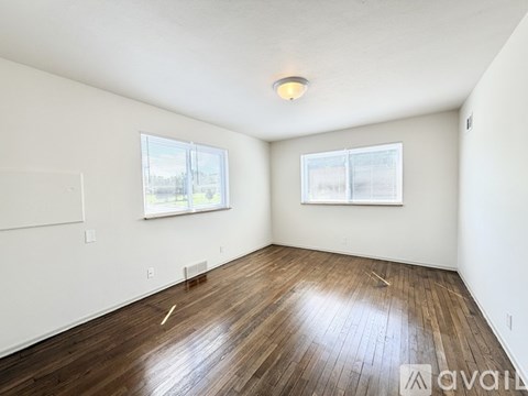 Empty room with wooden flooring and two windows.