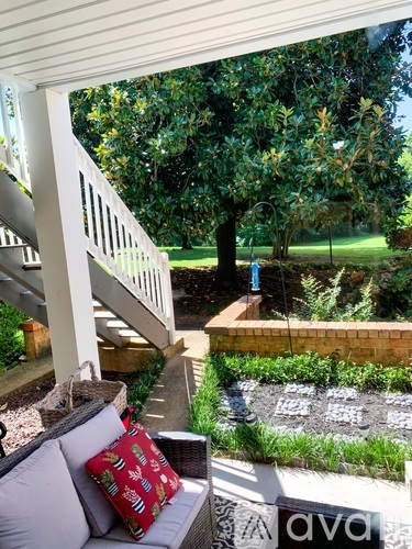 A patio with a couch and pillow with a view of a garden and trees.