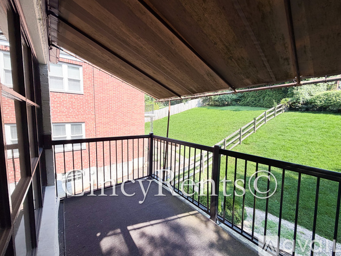 A balcony with a black railing and a view of a green lawn and a red building.