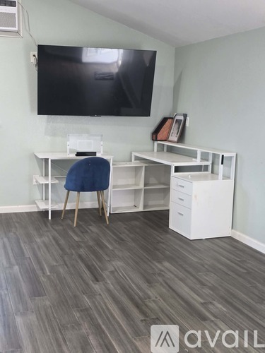 A room with a desk and a chair in front of a wall-mounted TV.