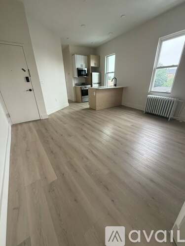 A spacious room with wooden flooring and a kitchenette in the background.