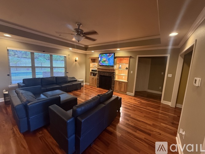 A living room with a black leather couch and a flat screen TV mounted on the wall.