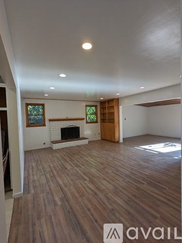 A spacious room with wooden flooring and a fireplace.
