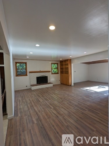 A spacious room with wooden flooring and a fireplace.
