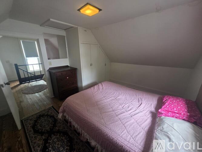 A bedroom with a pink bedspread and a rug on the floor.